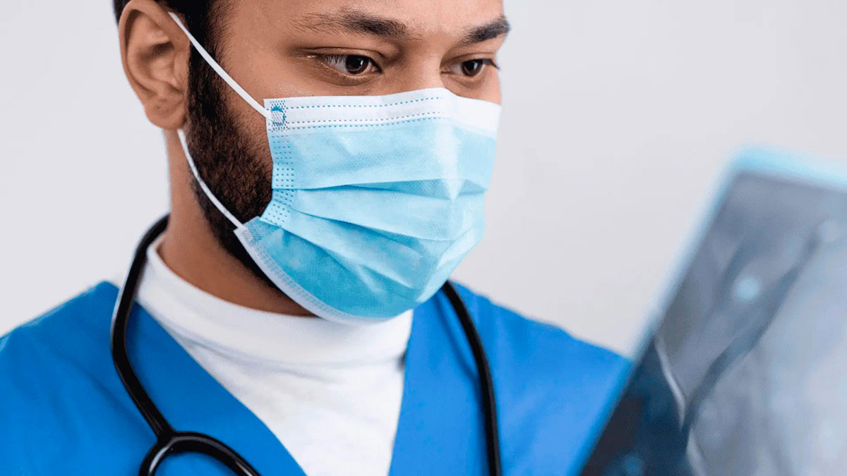 Médico de máscara cirúrgica e estetoscópio analisando exame de raio-x do pulmão para diagnóstico clínico.